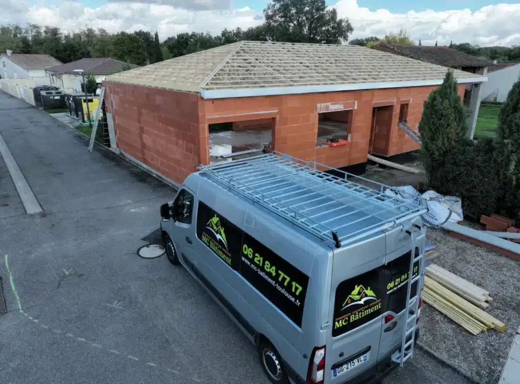 Maison en construction avec un van de chantier garé à l'avant, vue oblique.
